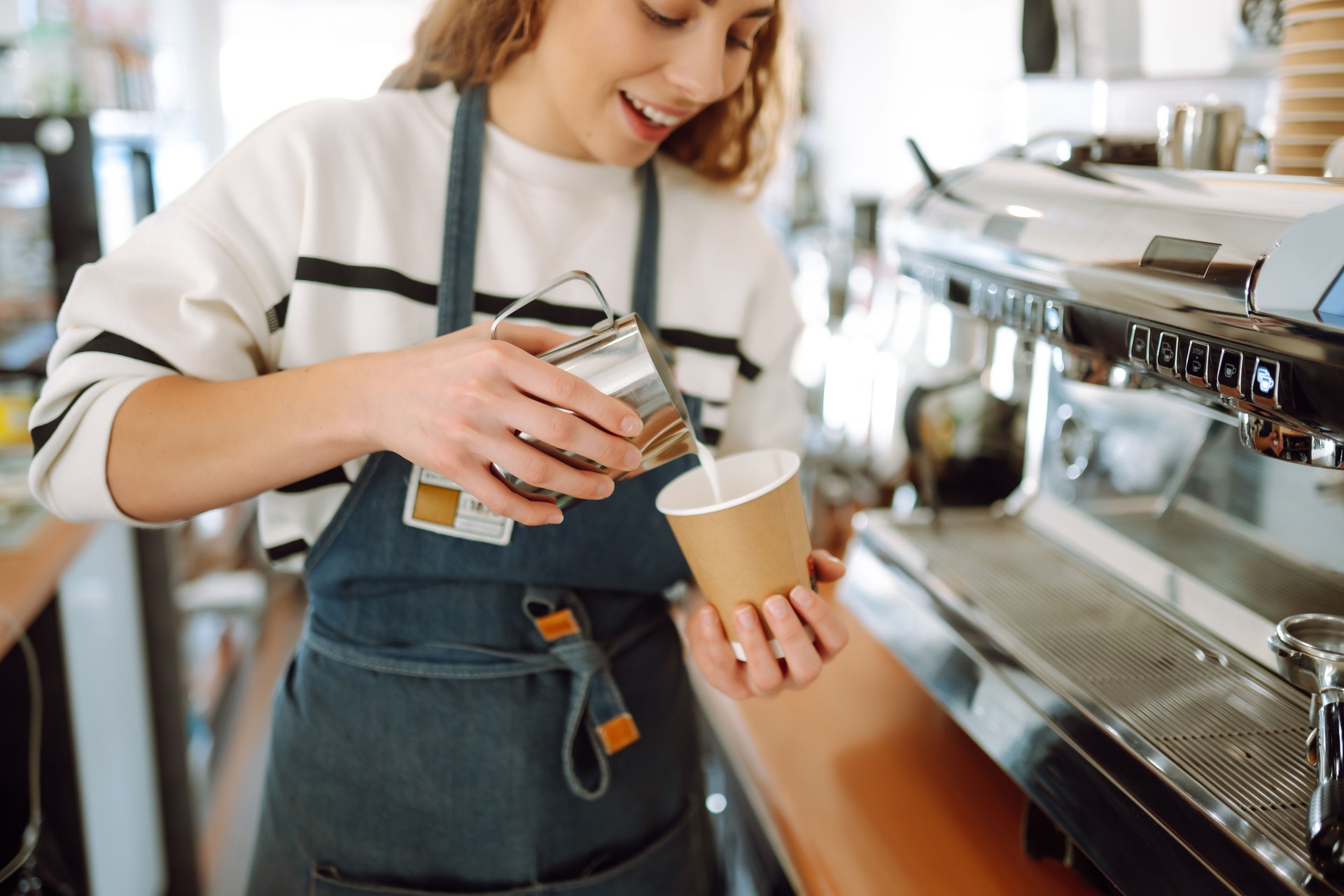 Barista holding cup getting fresh coffee that being brewed by the machine in cafe.